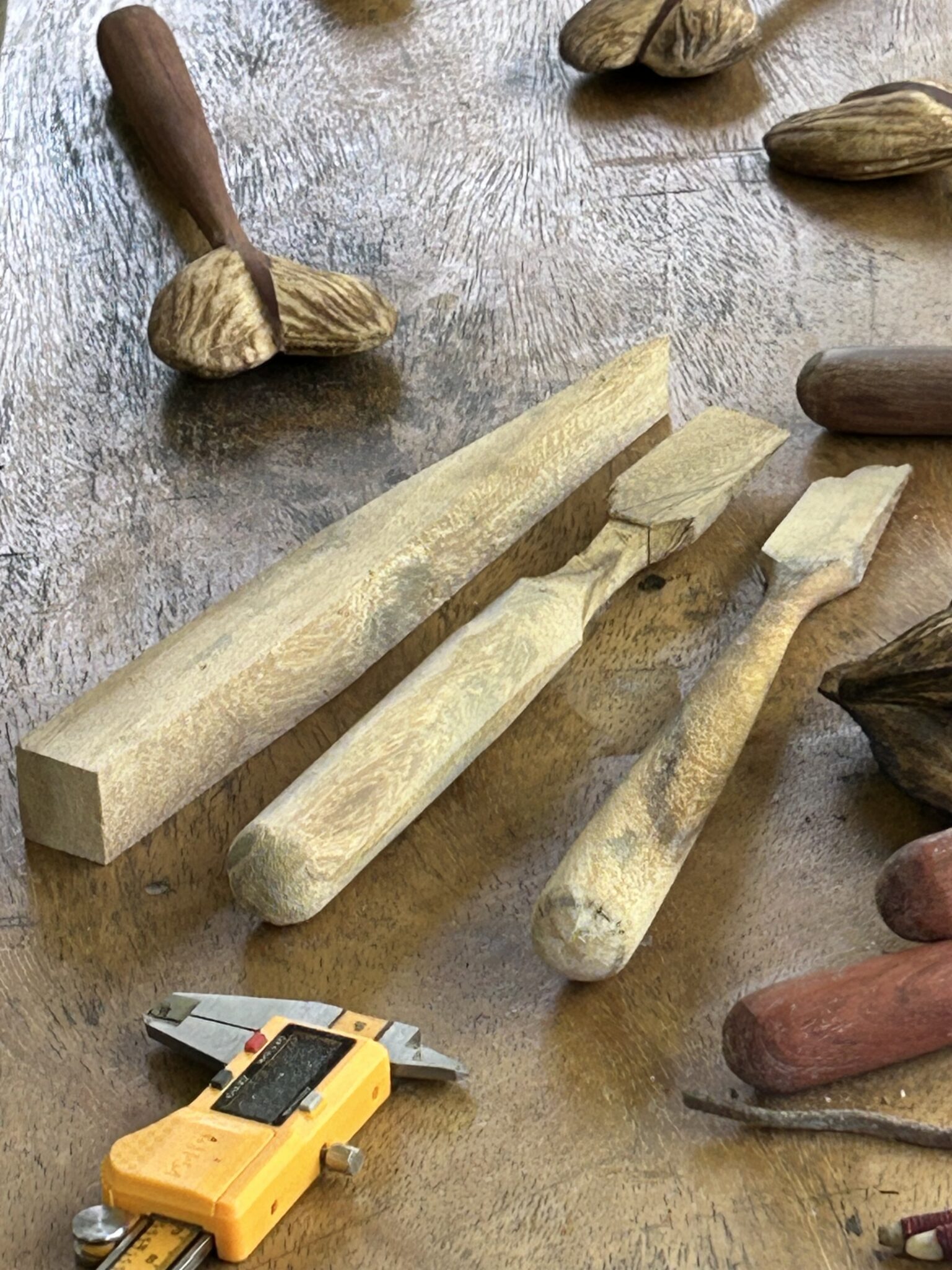 Handles at various stages of shaping alongside seeds and a caliper